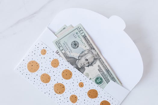 A polka dot envelope partially revealing US dollar bills on a white marble surface.